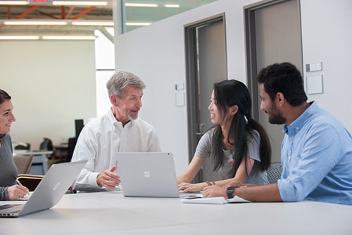 Faculty member and students talking and looking at laptops